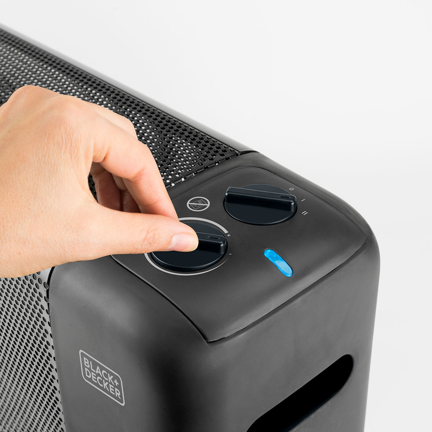 Dłoń przekręca pokrętło na czarnym grzejniku. Logo Black+Decker widoczne.