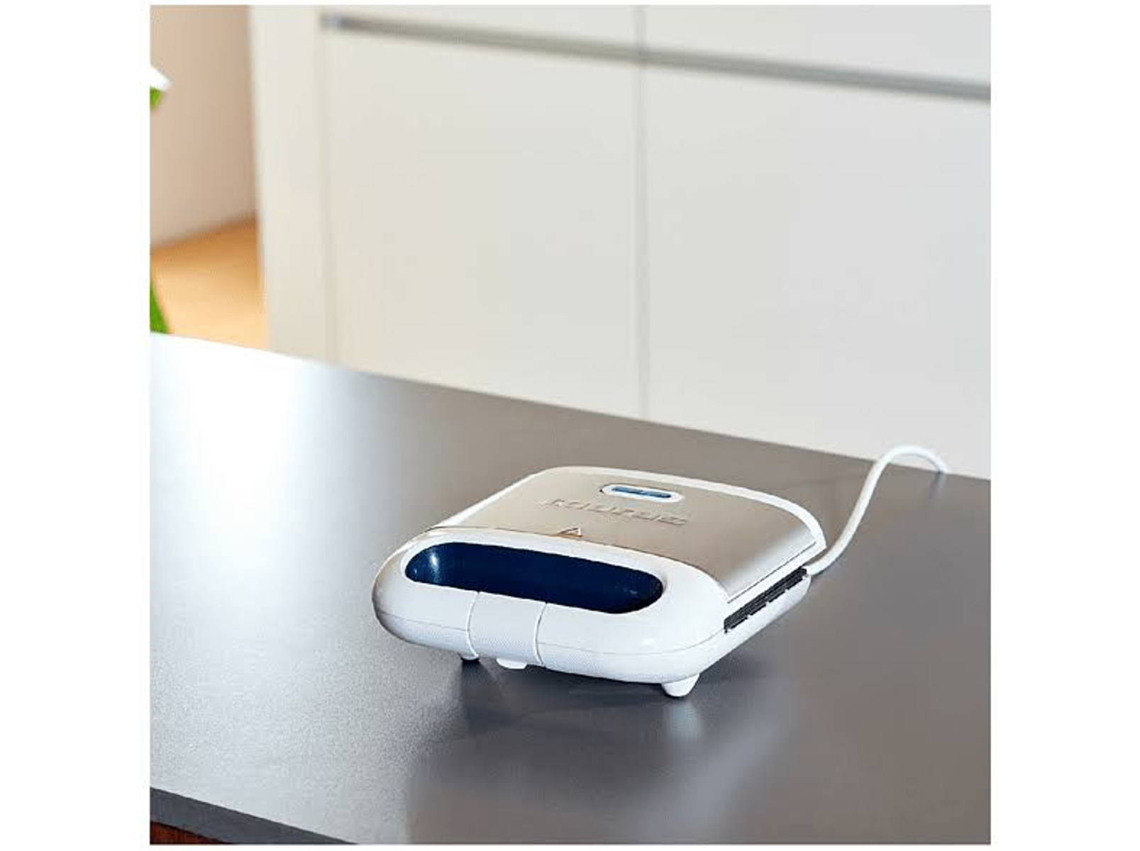 Srebrno-biała opiekacz do kanapek na szarej powierzchni. Tło to biała ściana.