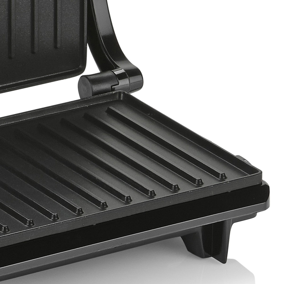 Una plancha panini negra, primer plano de la superficie de cocción con marcas de parrilla. La plancha está abierta.