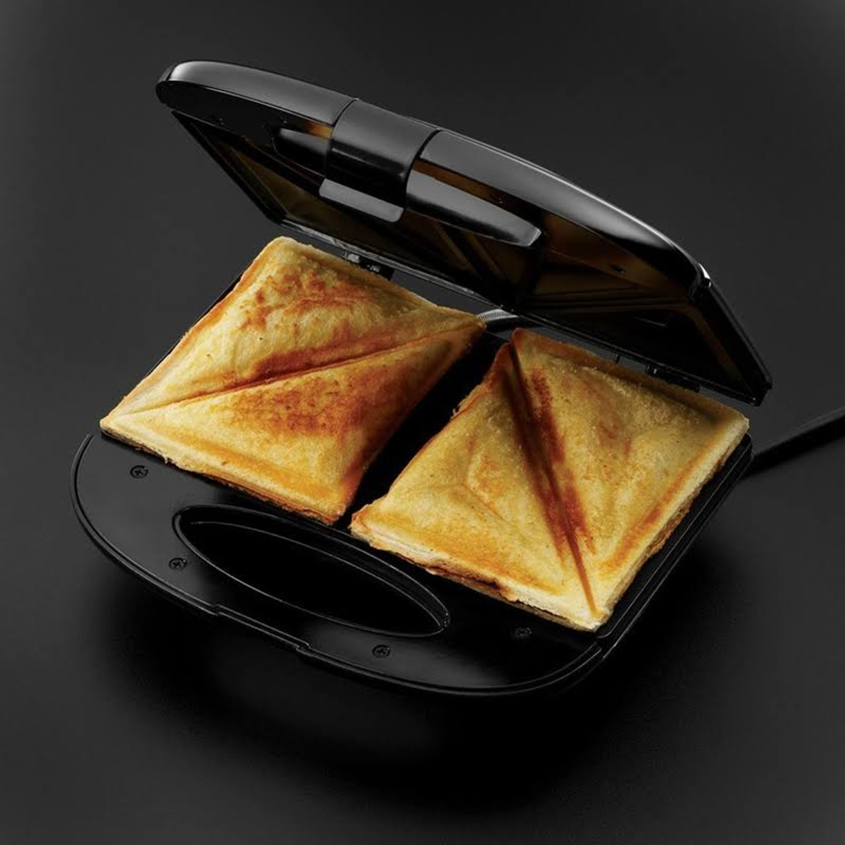 Sandwich-Toaster offen, zeigt zwei getoastete Sandwiches. Schwarz, dunkler Hintergrund.