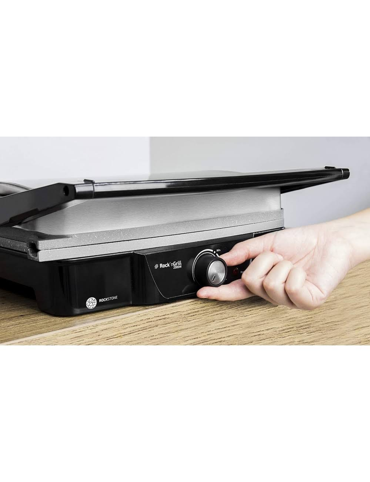 Ręka przekręca pokrętło na czarnym opiekaczu do panini na drewnianej powierzchni.