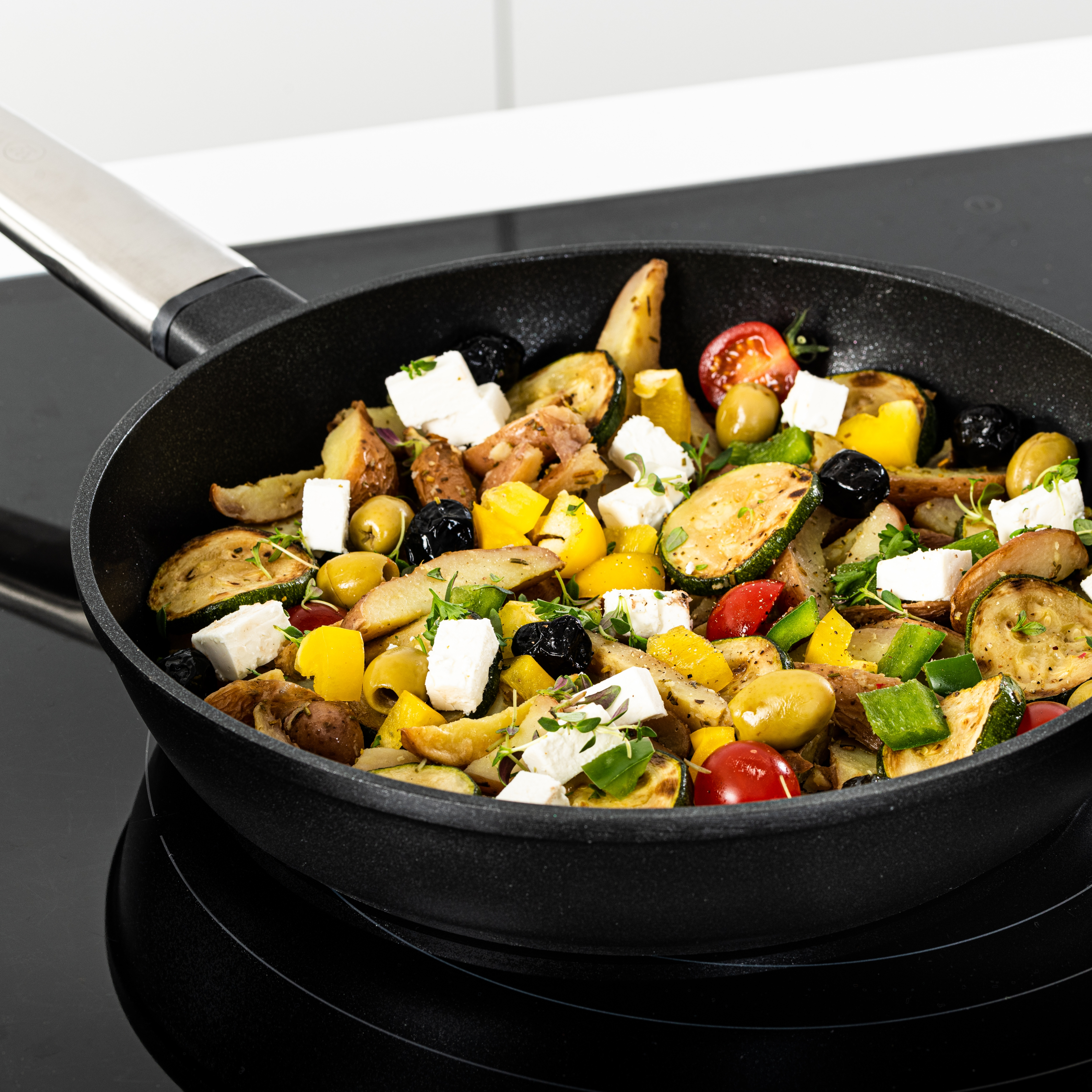 Pfanne mit gekochtem Gemüse, Feta und Oliven. Schwarze Pfanne auf schwarzem Herd.