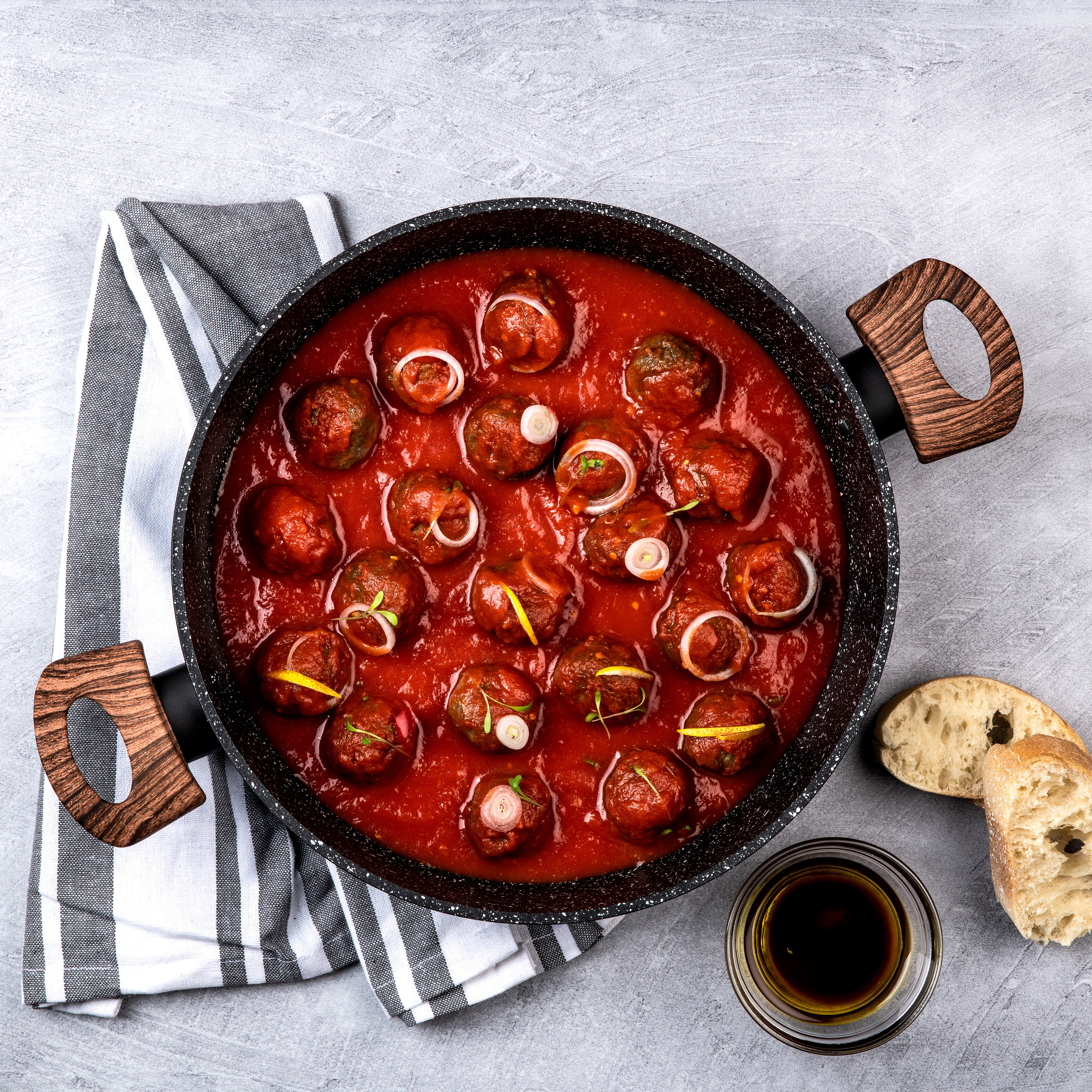 Draufsicht auf eine Pfanne mit Fleischbällchen in Tomatensauce, mit Zwiebeln garniert und Brot am Rand.