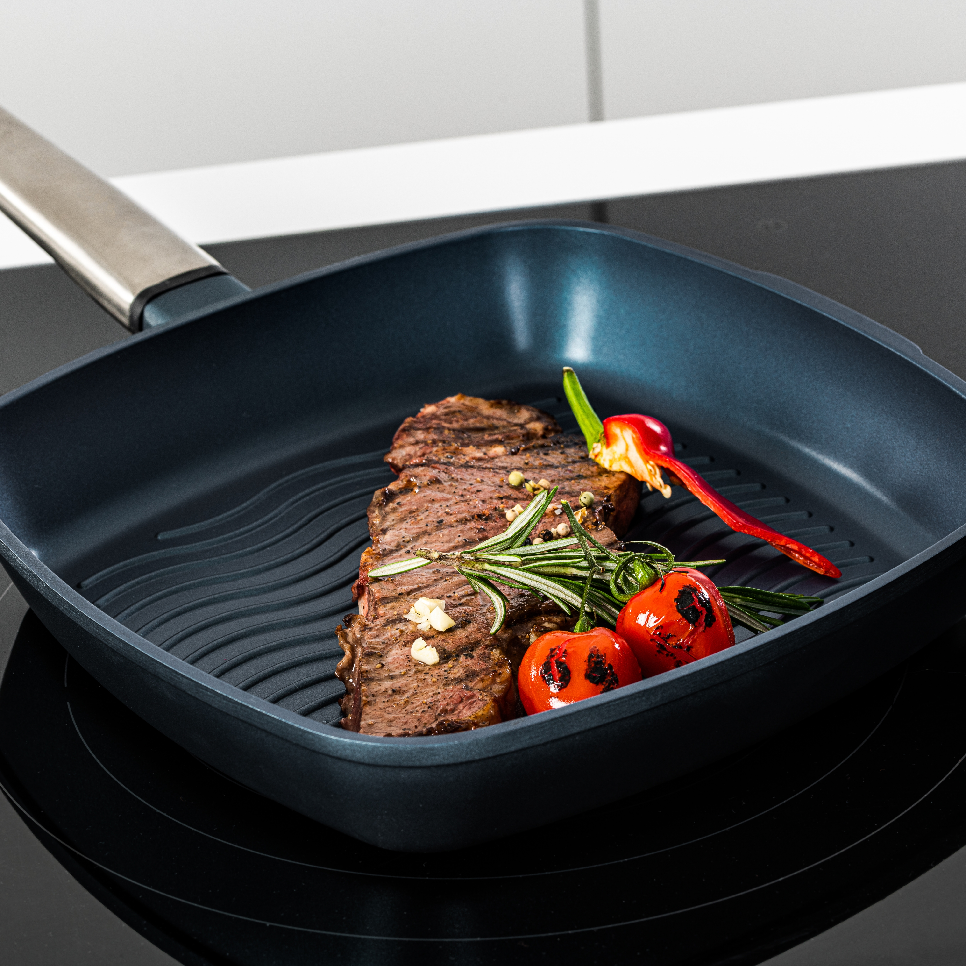 Gegrilltes Steak in einer Pfanne mit Tomaten, Rosmarin und Pfeffer. Pfanne steht auf dem Herd.