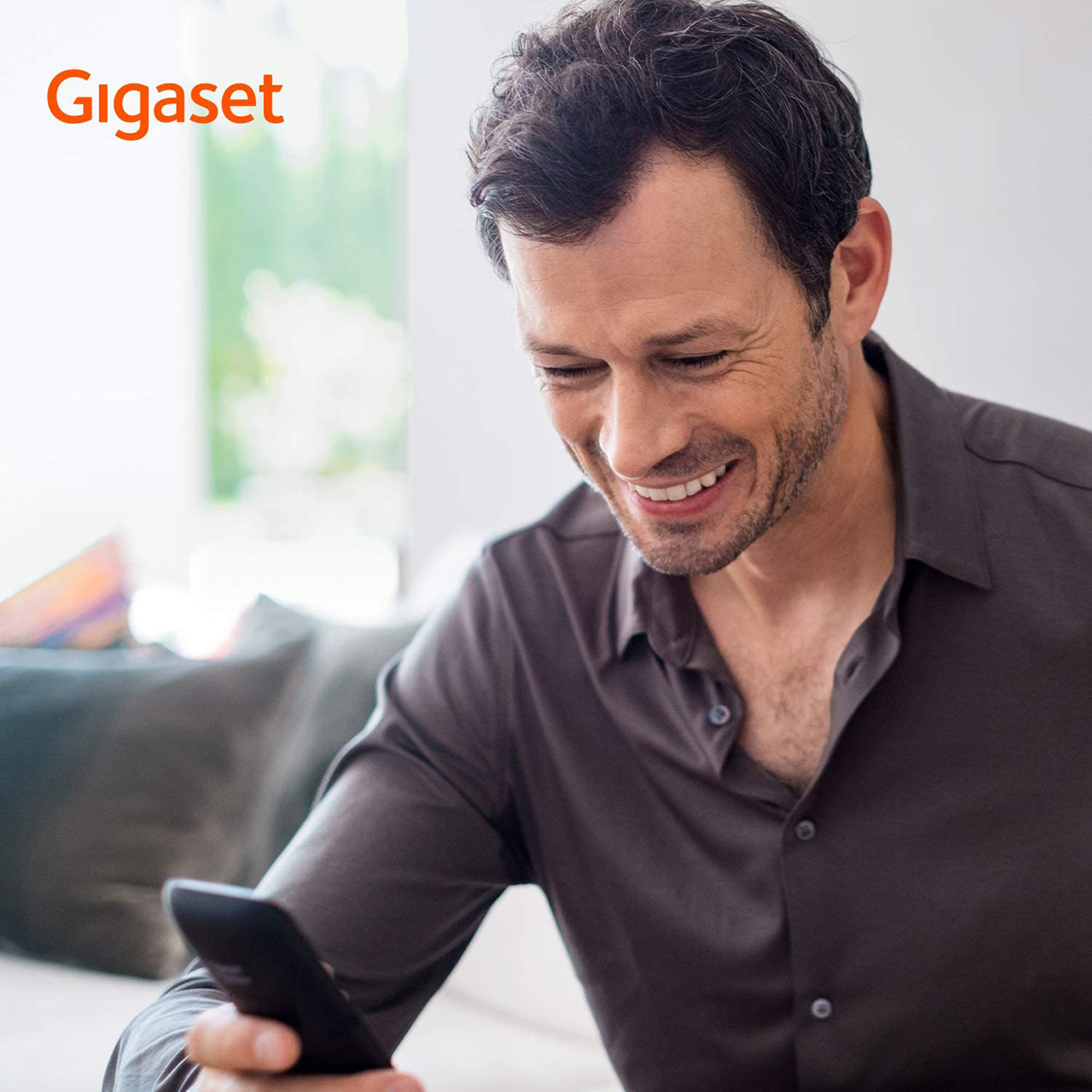 Ein Mann schaut lächelnd auf sein Handy. Das Gigaset-Logo ist oben links.