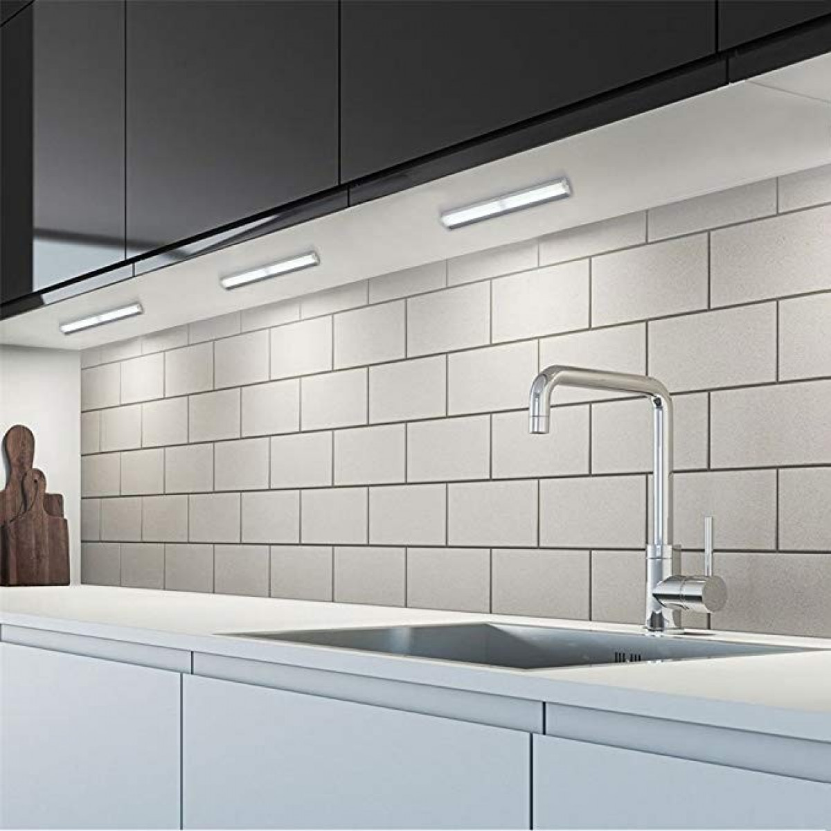 Een moderne keuken met witte kasten, een roestvrijstalen spoelbak en een witte tegelachterwand met lampen.