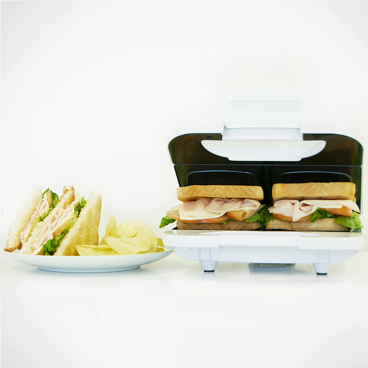 Máquina para hacer sándwiches con sándwiches y plato. Dos sándwiches cocinándose, patatas fritas y sándwich en plato.