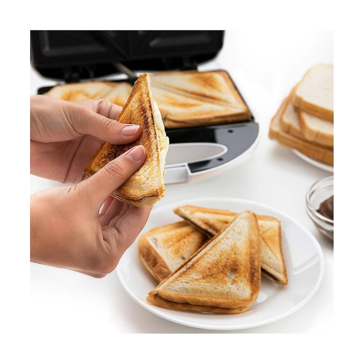 Mani che tengono un toast. Piatto con panini e ciotola di crema spalmabile.