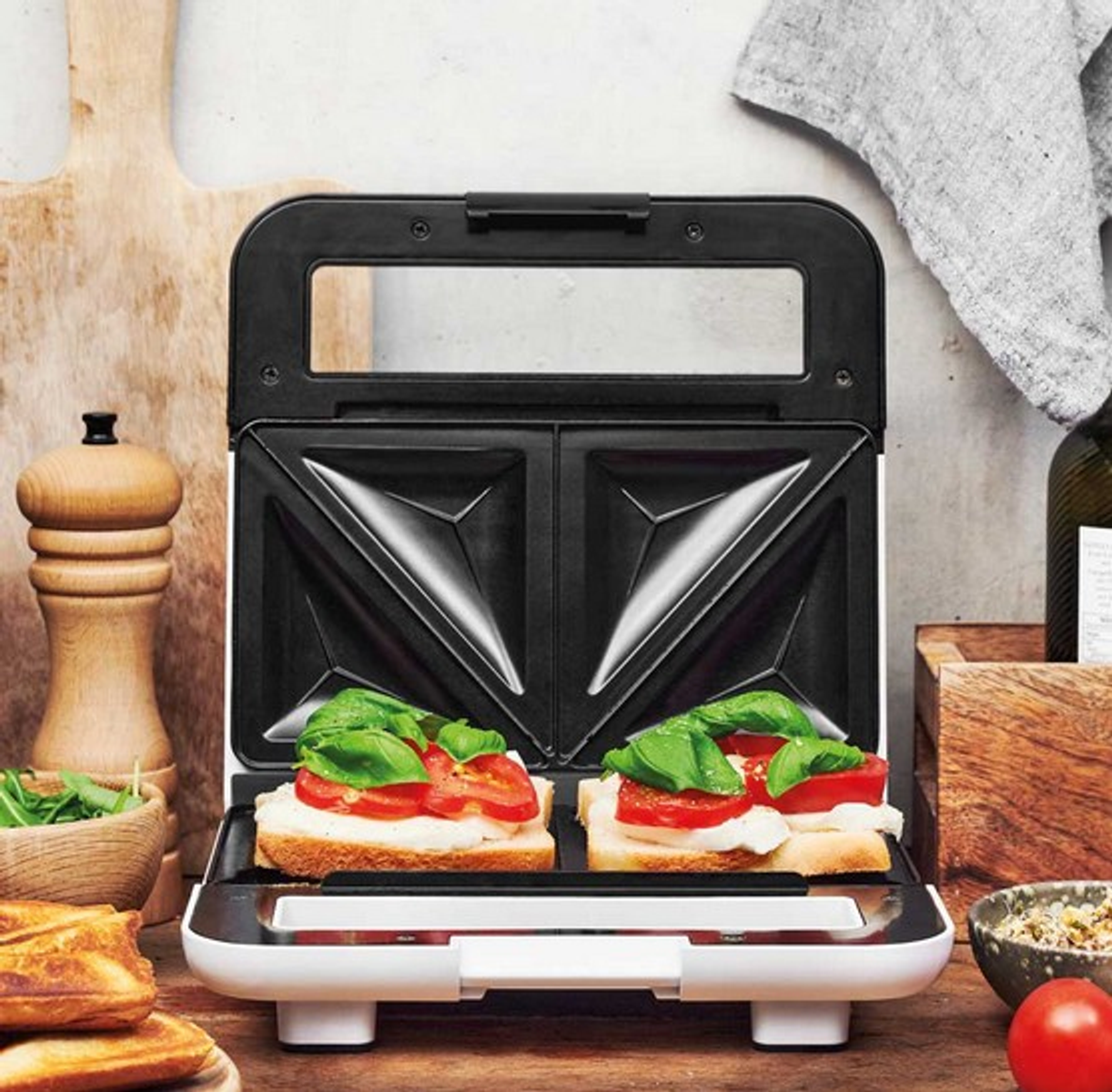 Offener Sandwichmaker mit zwei Sandwiches: Brot, Tomate, Basilikum und Käse.