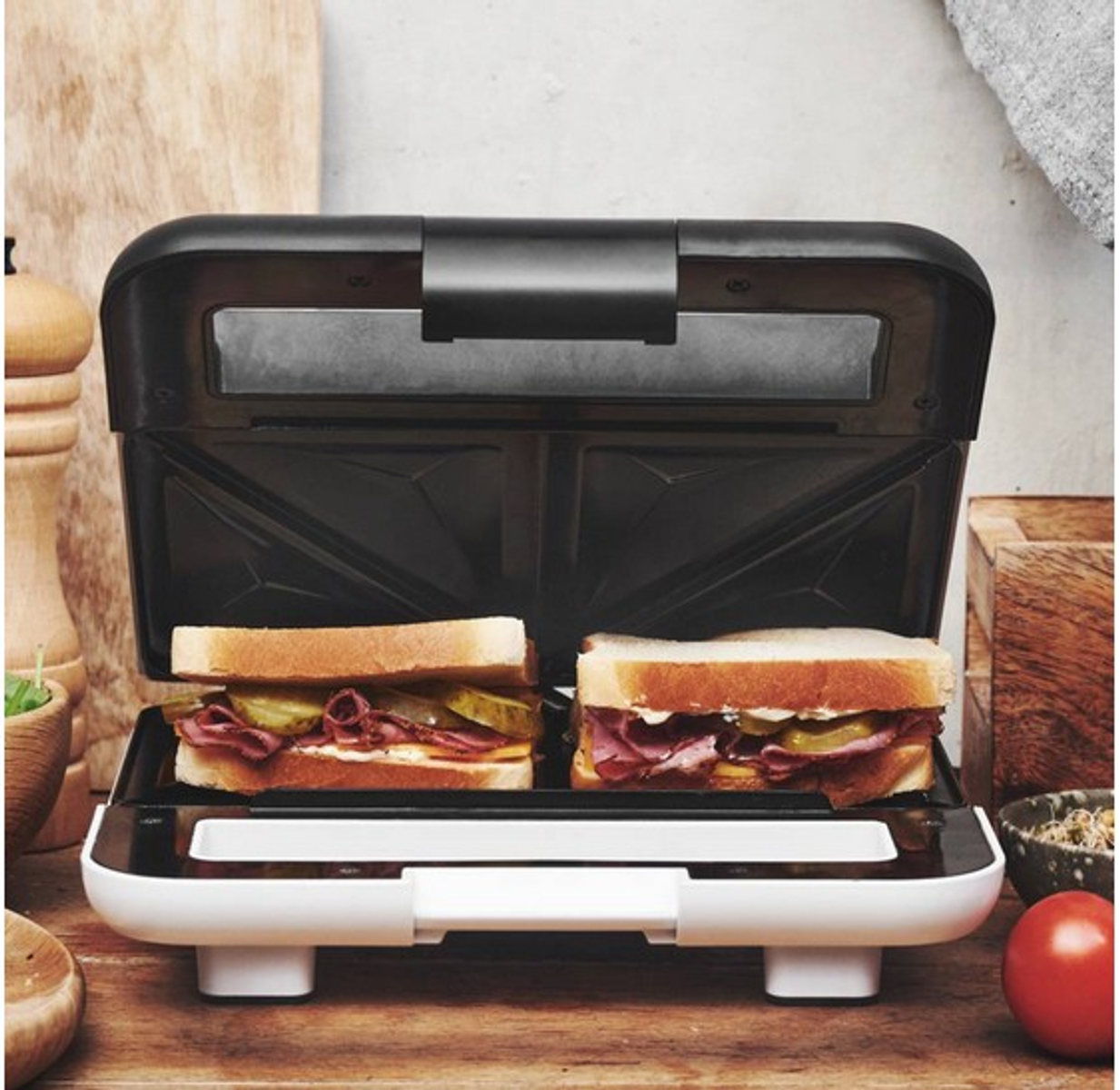 Ein Sandwichmaker mit zwei Sandwiches. Die Sandwiches haben Brot, Gurken und Fleisch.