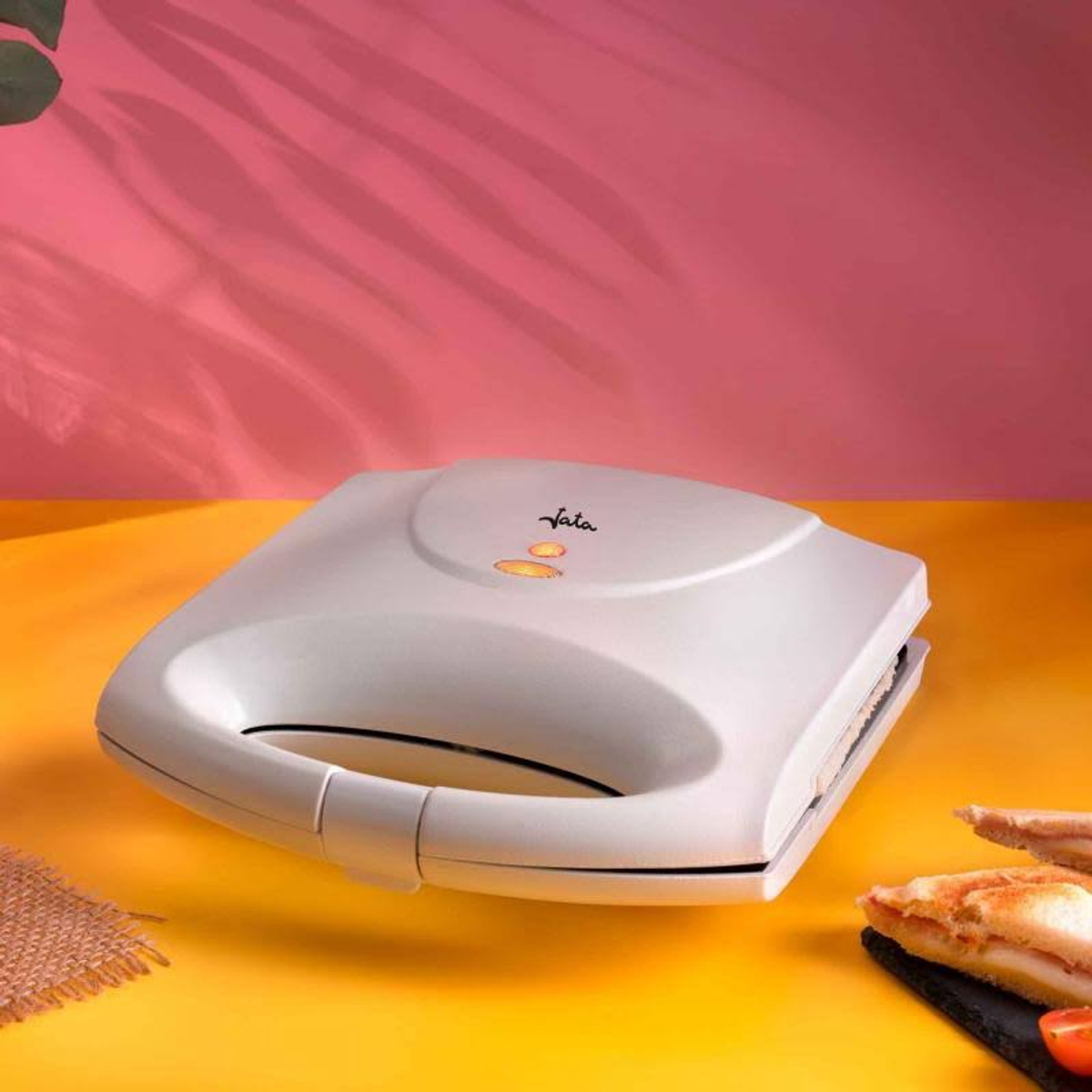 Sandwich maker bianco su una superficie gialla, con sfondo rosso e rosa. Panino davanti.