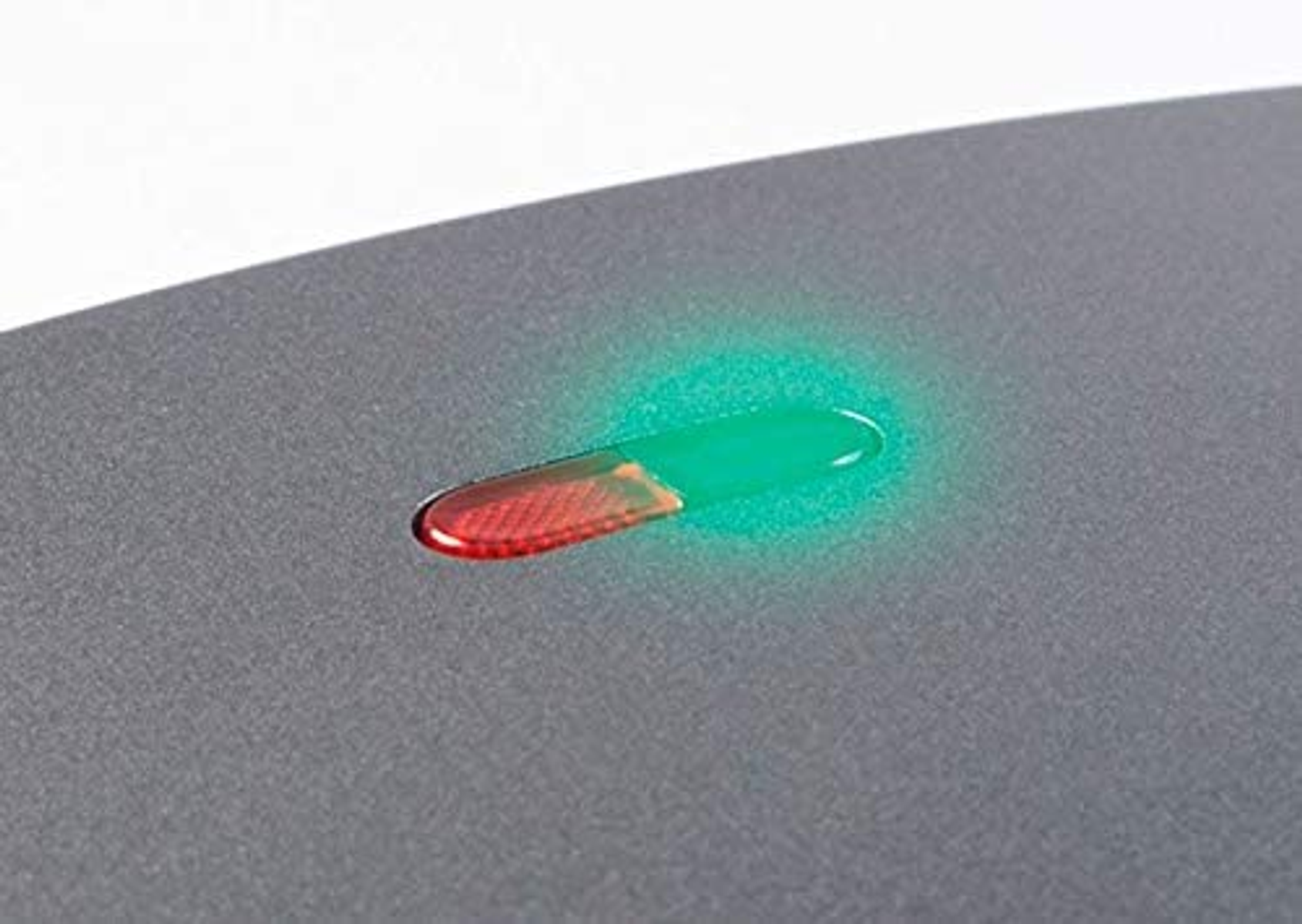 Primer plano de una luz indicadora verde y roja en una sandwichera. Fondo gris.