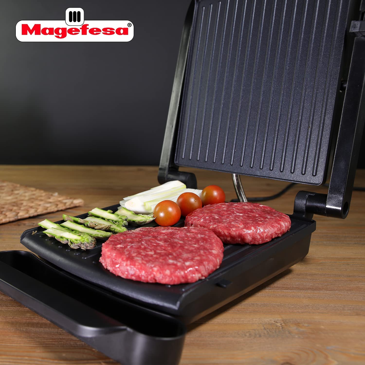Parrilla Magefesa con hamburguesas crudas, espárragos y tomates. Superficie de madera.