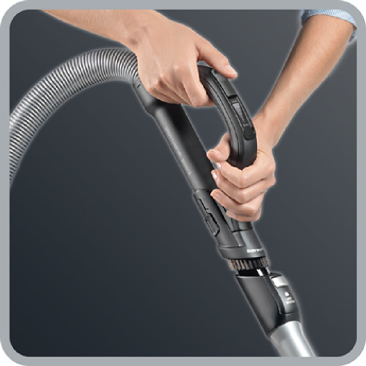 Dłonie trzymające uchwyt odkurzacza. Uchwyt jest czarny i ma szczotkę.