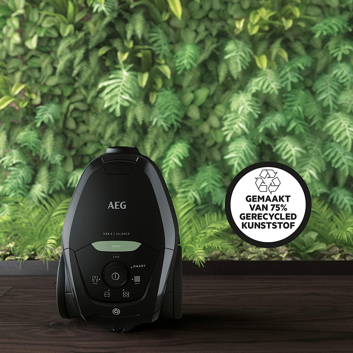 Czarny odkurzacz AEG na drewnianej podłodze, zielone tło ściany roślin i odznaka z tworzywa sztucznego z recyklingu.