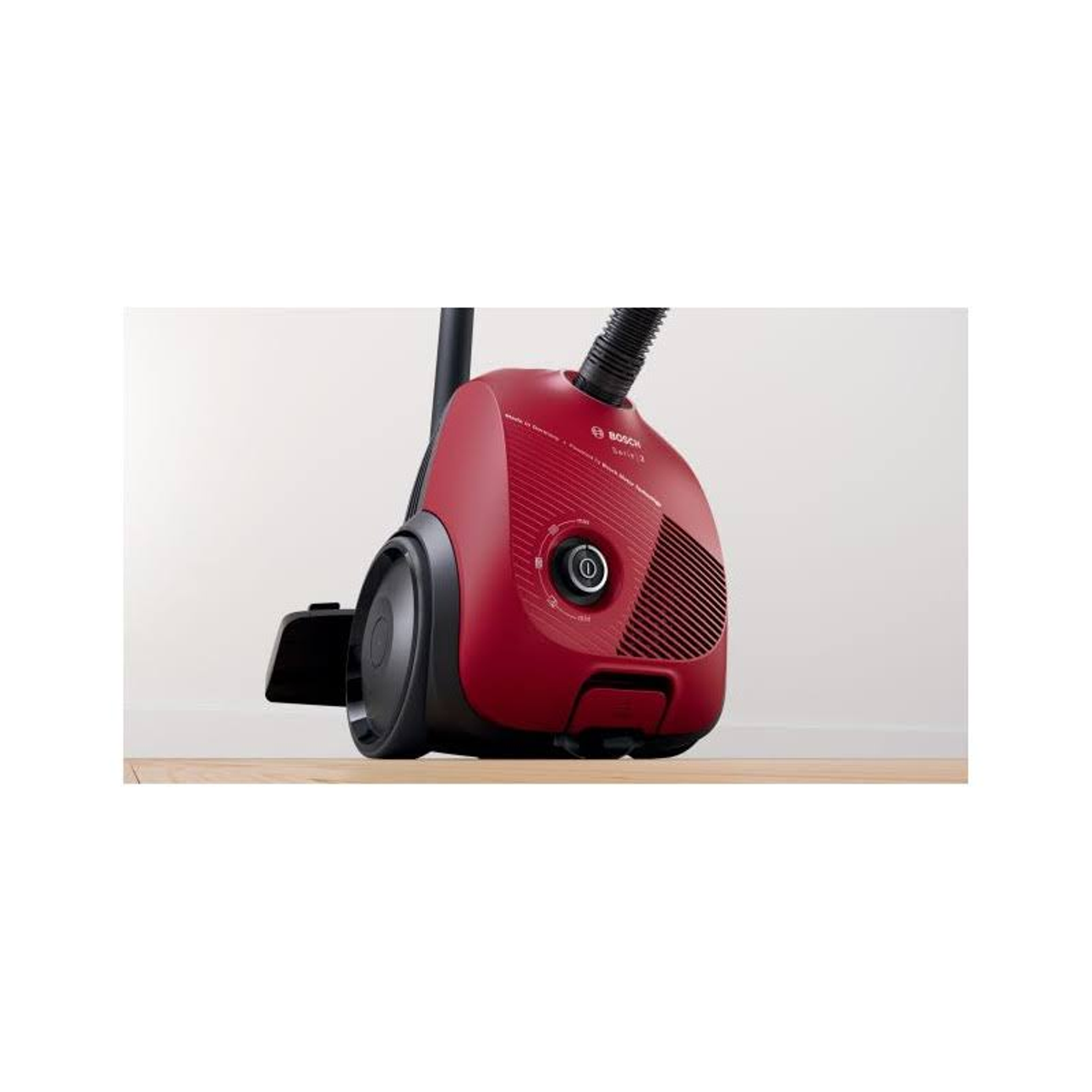 Czerwony i czarny odkurzacz na drewnianej podłodze, na tle białej ściany.