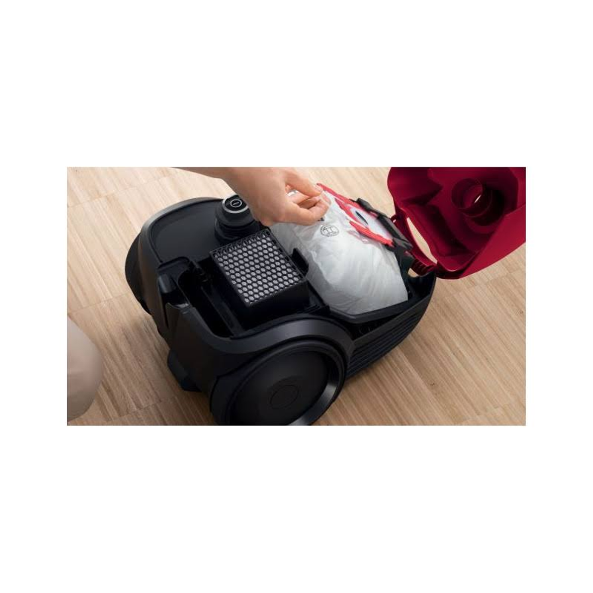 Odkurzacz, otwarty, pokazujący filtr i worek. Ręka sięga po worek.