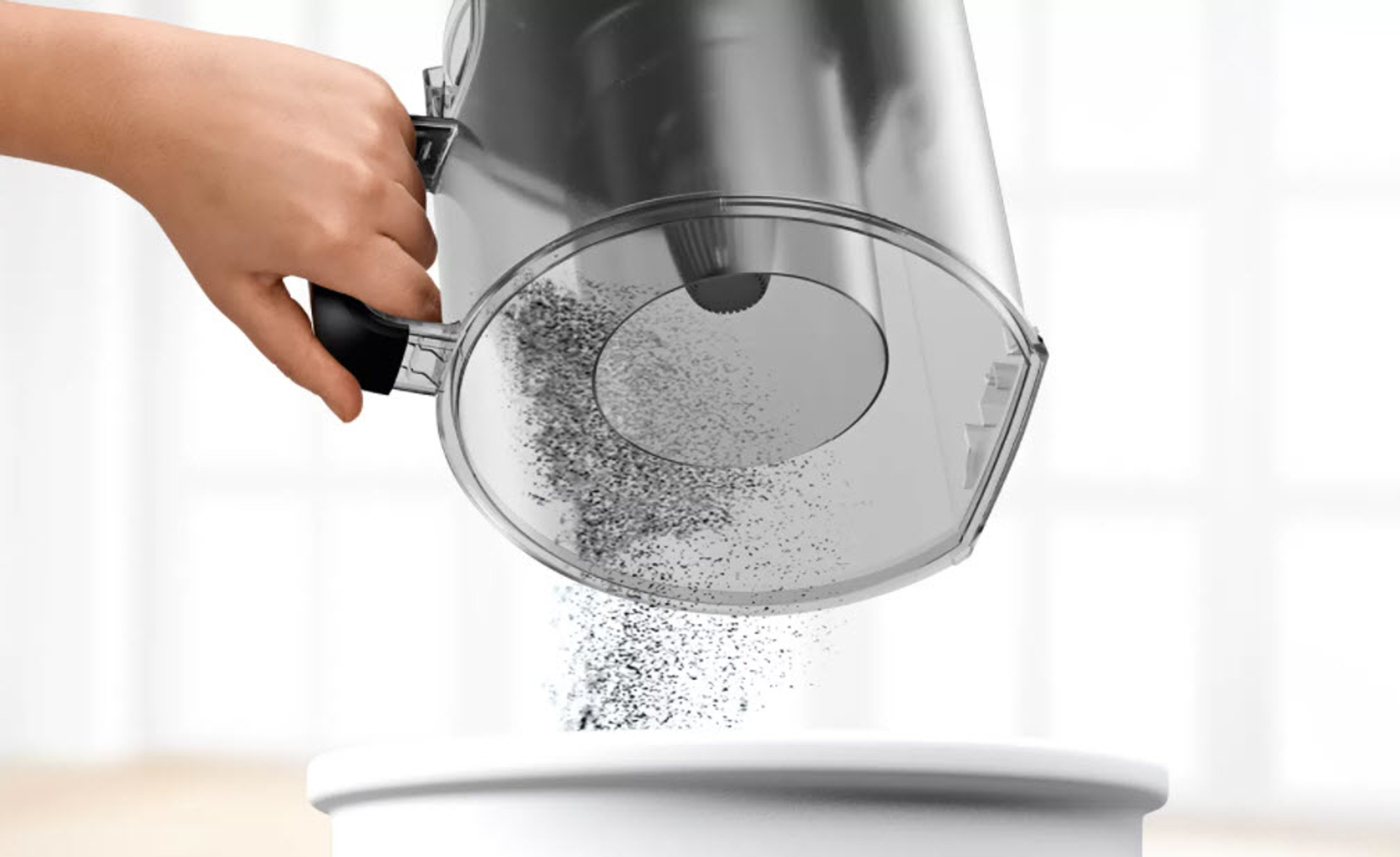 Ręka wylewa pył z przezroczystego pojemnika próżniowego do białego pojemnika.