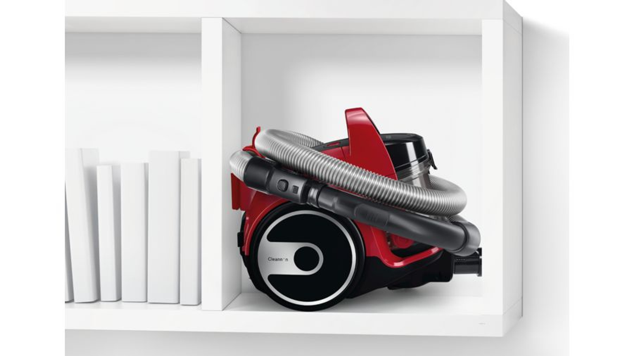 Czerwony odkurzacz przechowywany na białej półce. Wąż jest owinięty wokół odkurzacza.