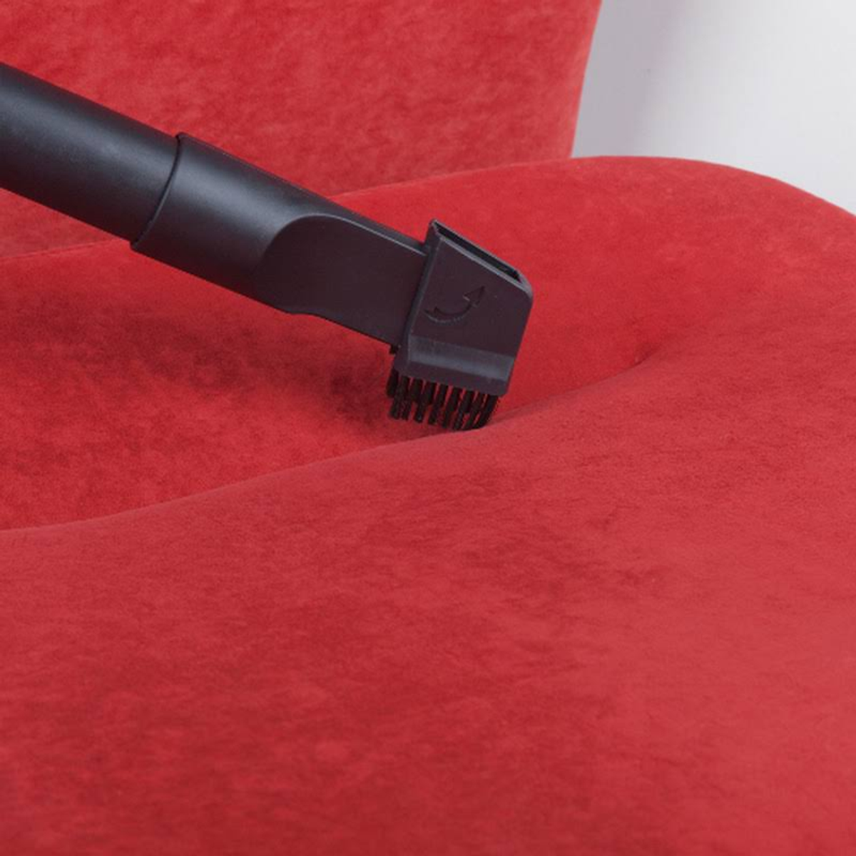 Un accesorio de aspiradora negro limpiando un sofá rojo. El cepillo está en contacto con la tela.