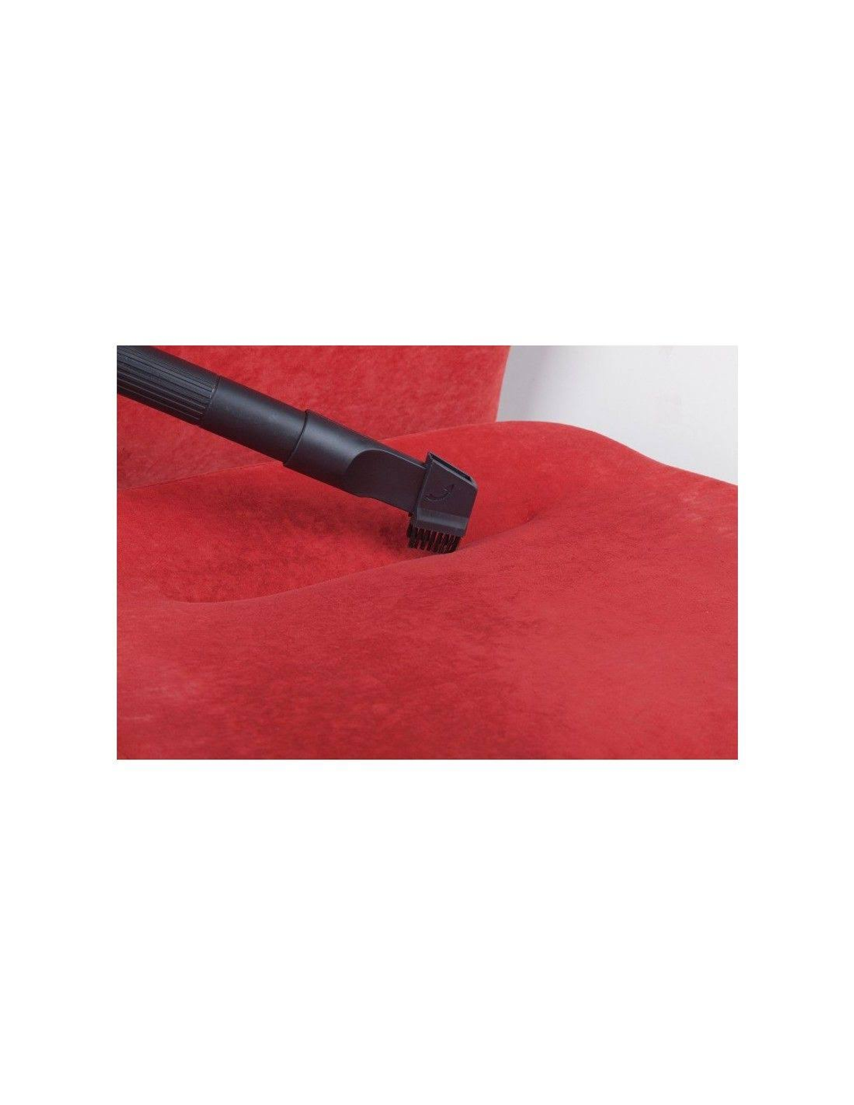 Una boquilla de aspiradora limpia una silla roja. El fondo es una pared blanca.