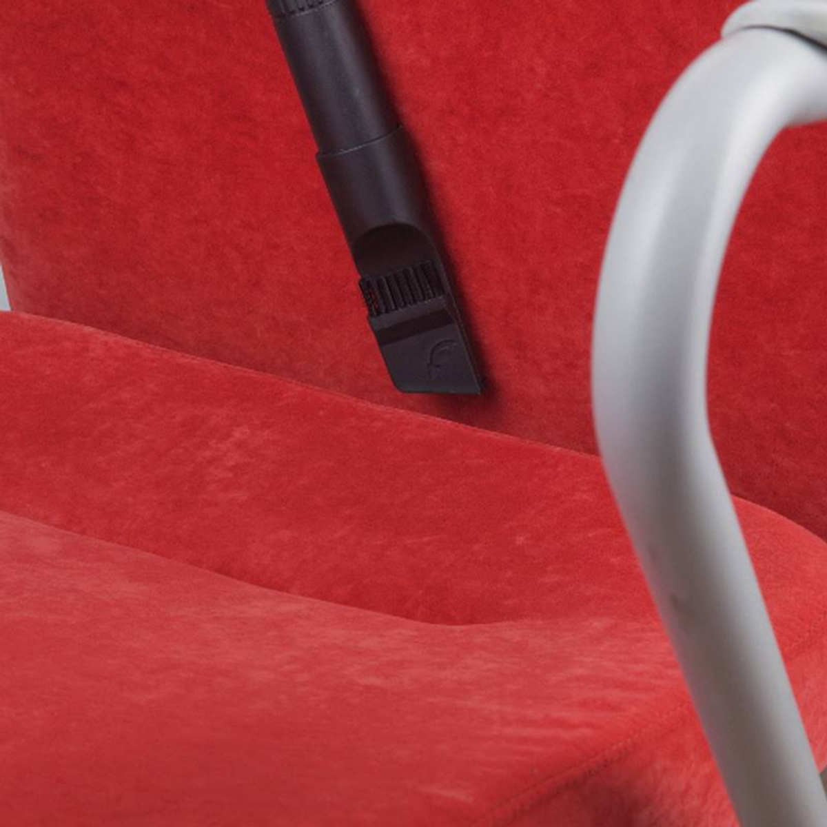 Aspirando un sofá rojo. Cabezal de vacío negro. Tubo plateado. Fondo beige.