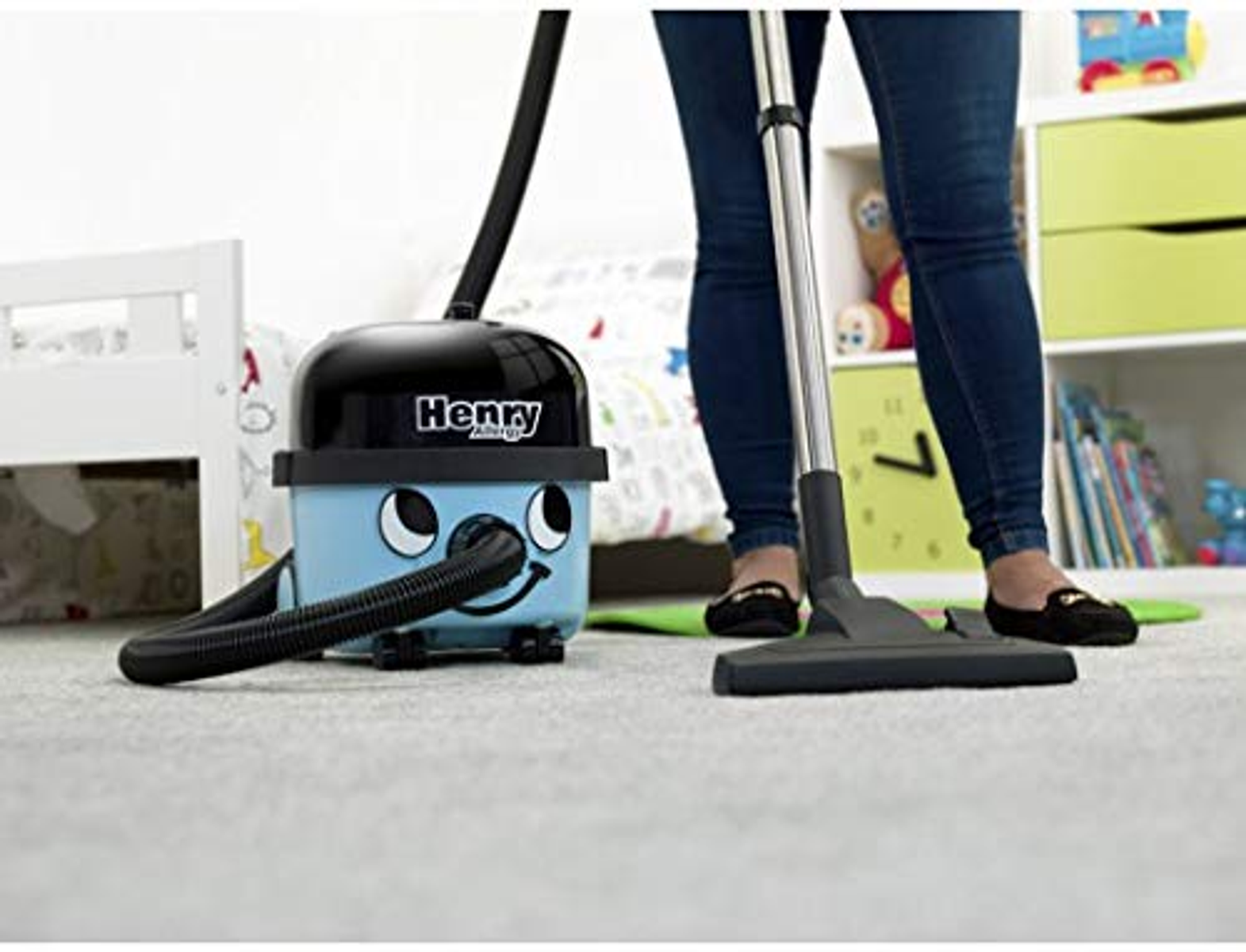 Niebieski odkurzacz Henry używany na podłodze pokrytej dywanem. Widoczna jest osoba.