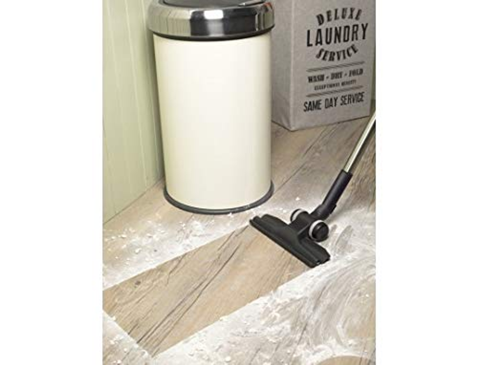 Biały kosz na śmieci ze srebrną pokrywą i odkurzacz na drewnianej podłodze.