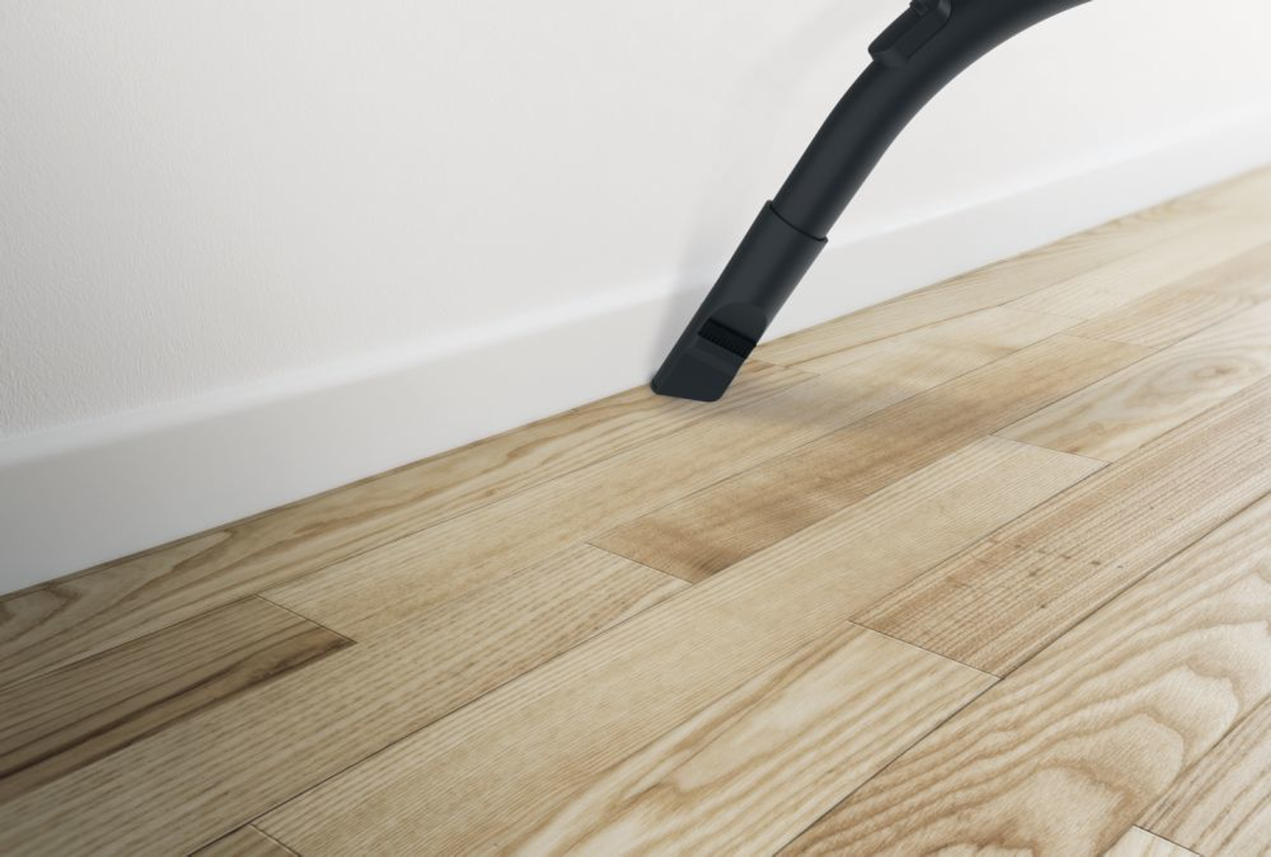 Dysza odkurzacza czyszcząca drewnianą podłogę w pobliżu białej ściany i listwy przypodłogowej.