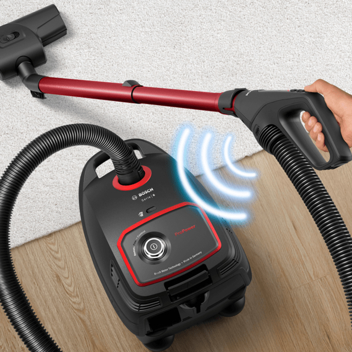 Czarny odkurzacz z czerwonymi akcentami, osoba trzymająca uchwyt, czyszcząca biały dywan.