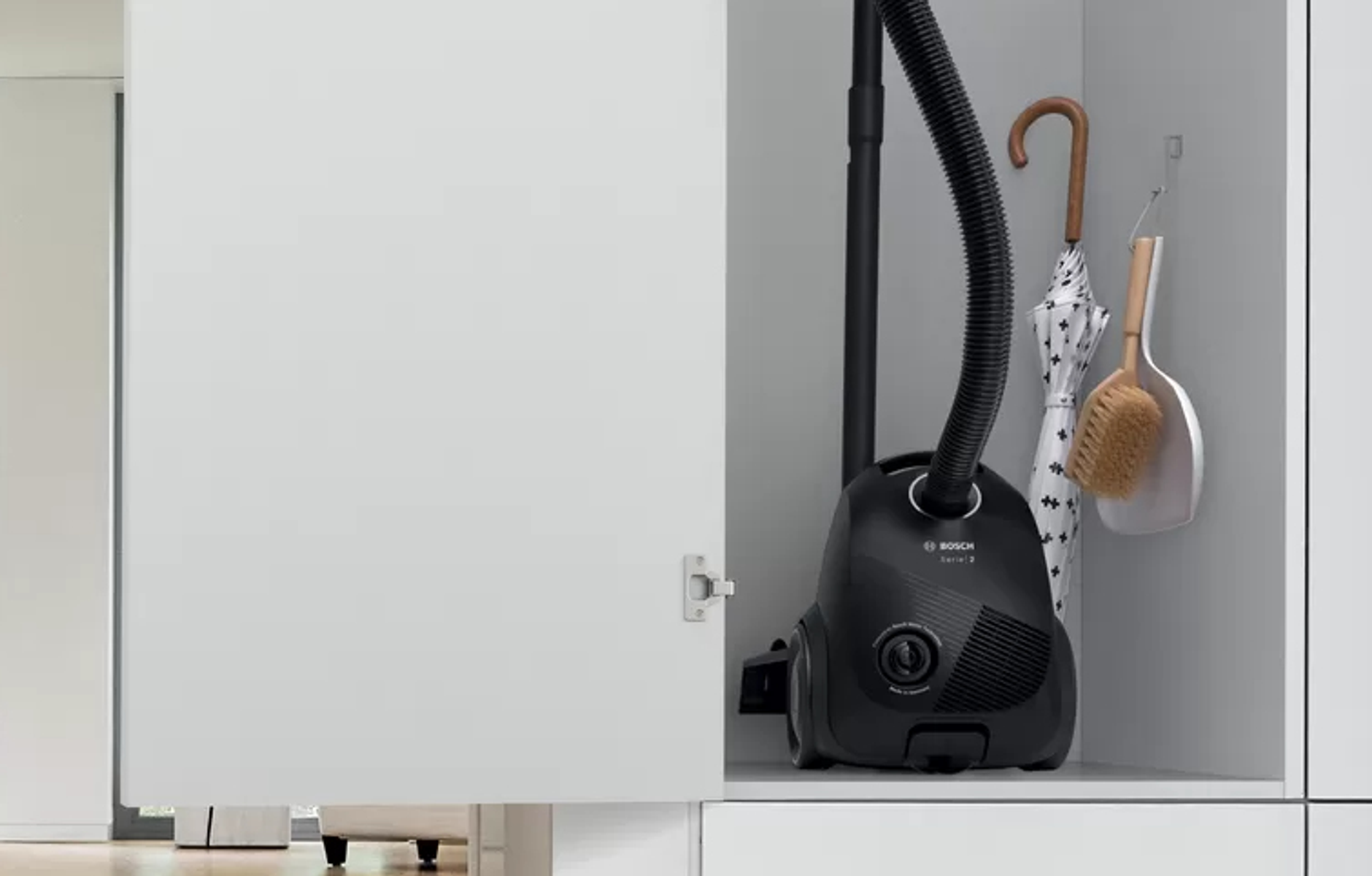 Czarny odkurzacz wewnątrz białej szafki z parasolem i szczotką.