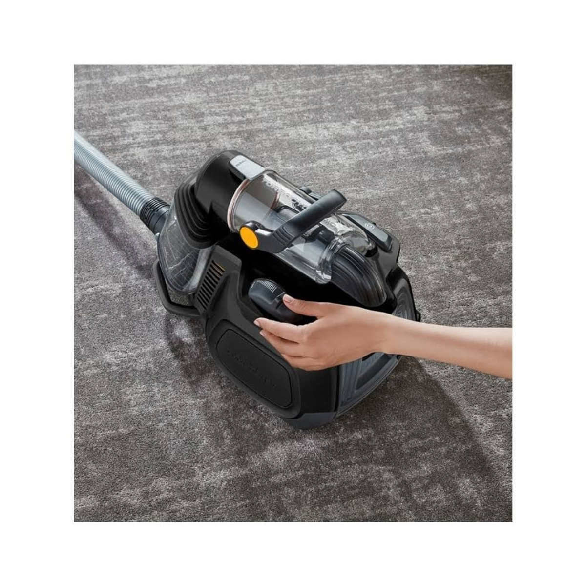Ein schwarzer Staubsauger auf einem grauen Teppich. Eine Hand berührt die Maschine.