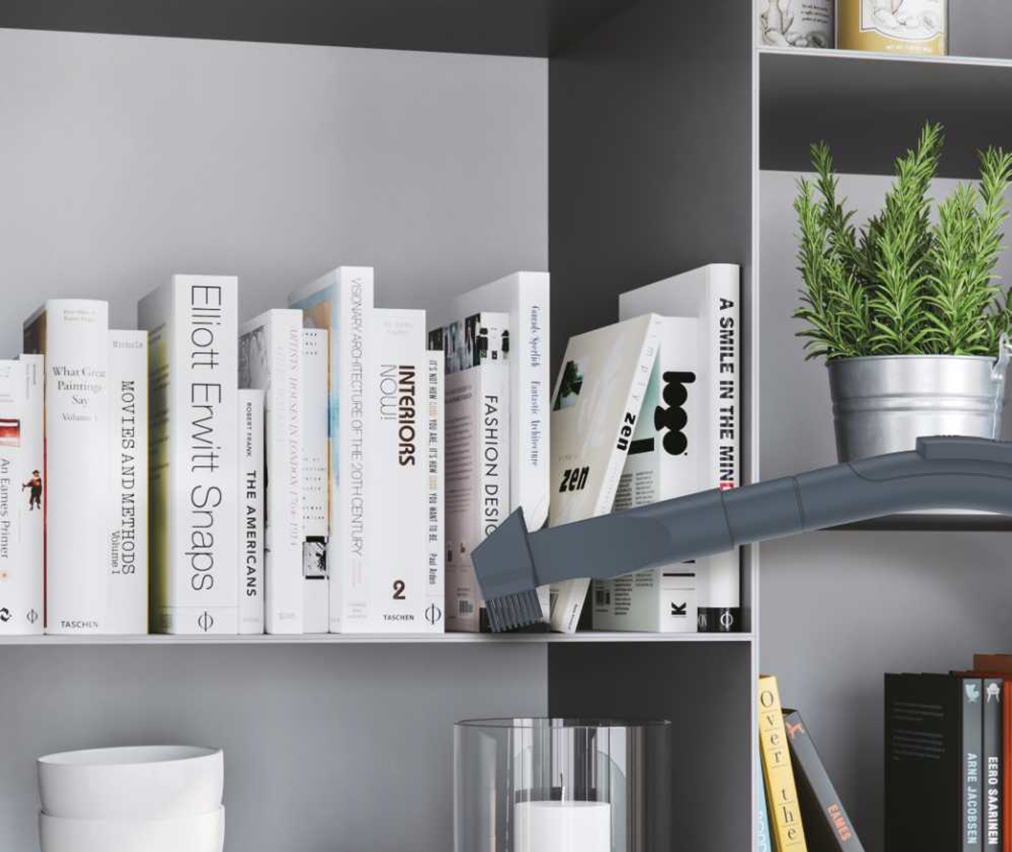 Odkurzacz czyści półkę z książkami i rośliną na górnej półce.