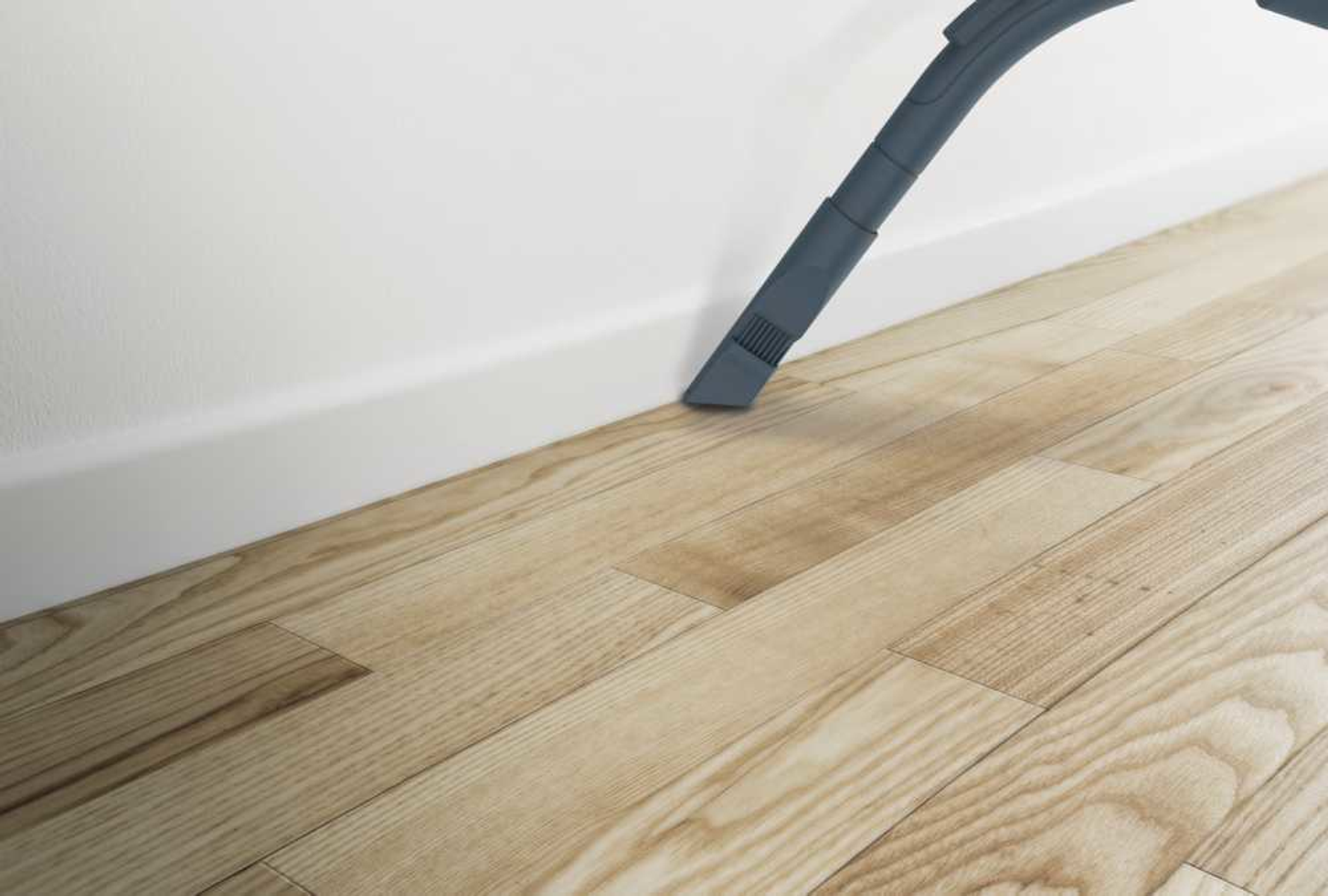 Zbliżenie dyszy odkurzacza spoczywającej na drewnianej podłodze obok białej ściany.