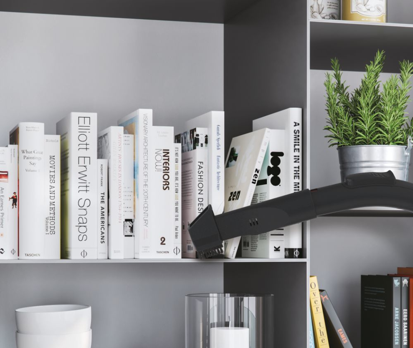 Dysza odkurzacza czyszcząca półkę z książkami i rośliną.