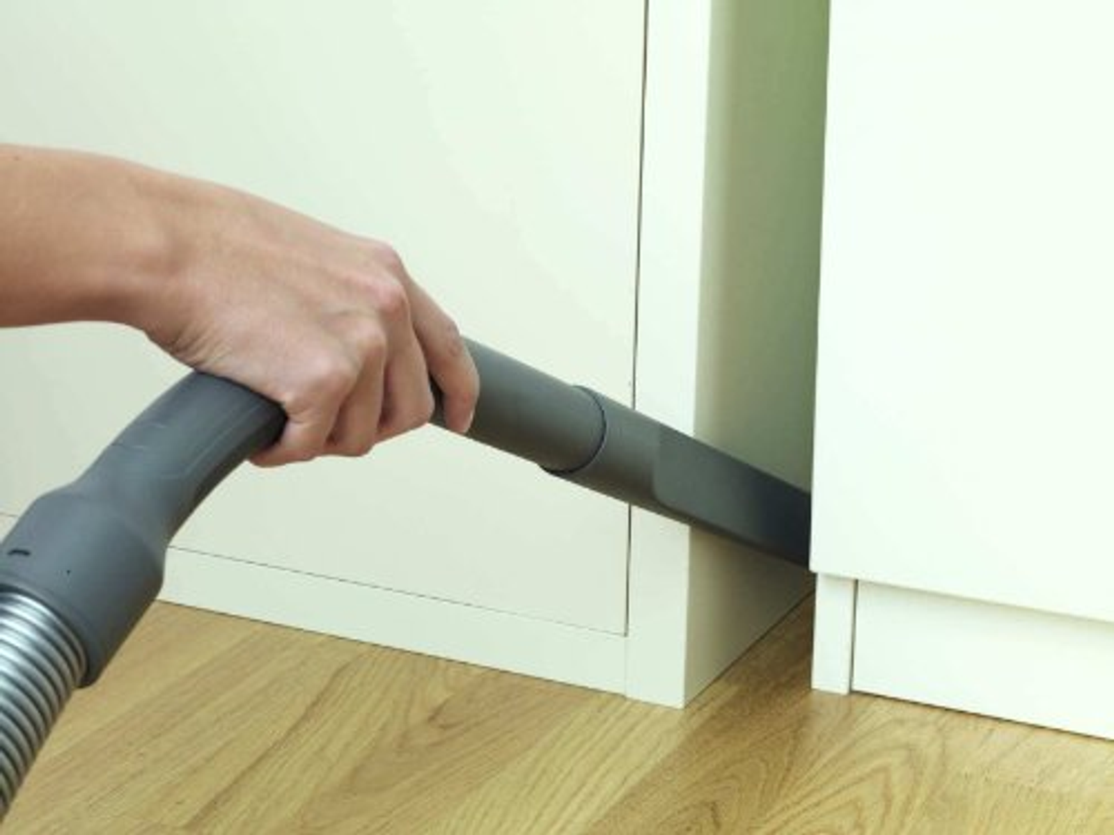 Ręka używająca węża odkurzacza. Czyszczenie szafki. Drewniana podłoga. Beżowe szafki.