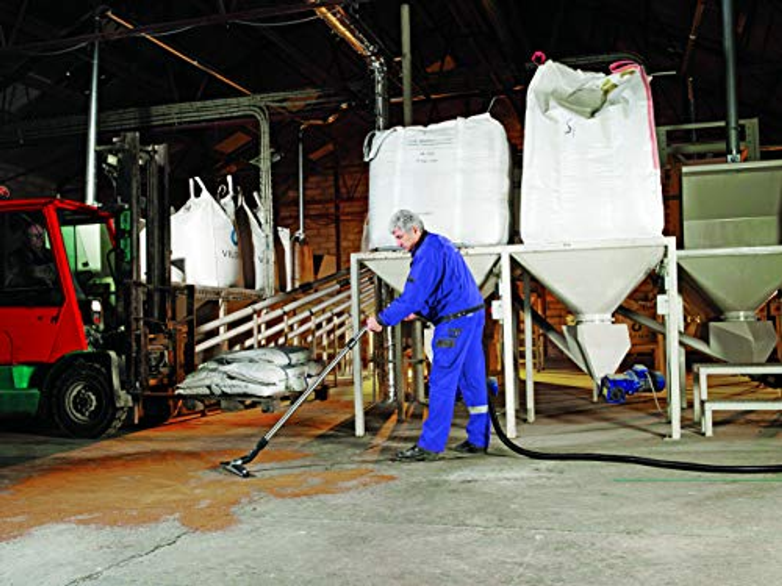 Un uomo in tuta blu che aspira un pavimento di cemento in un ambiente industriale.