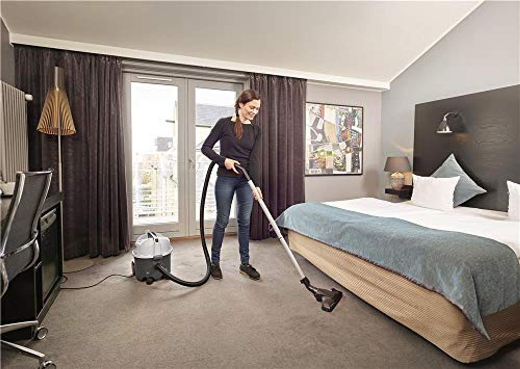 Donna aspira una camera d'albergo con finestra e letto.