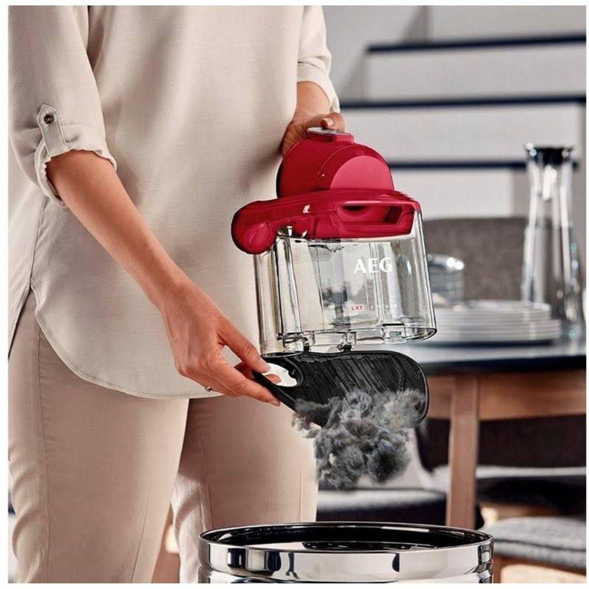 Osoba opróżniająca mały czerwony odkurzacz do stalowego pojemnika.