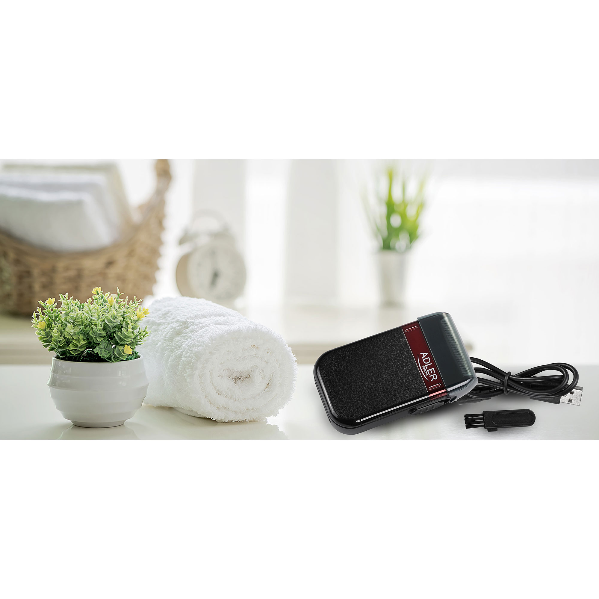 Czarna i czerwona golarka, ręcznik, roślina i kosz na białym stole w jasnym pokoju.