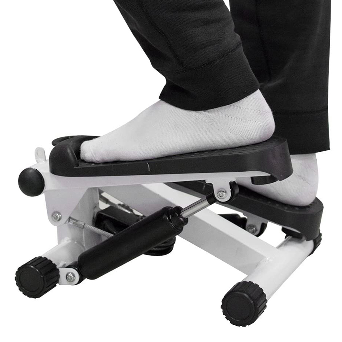 Pies de persona en una máquina de step blanco y negro, calcetines blancos, fondo blanco.