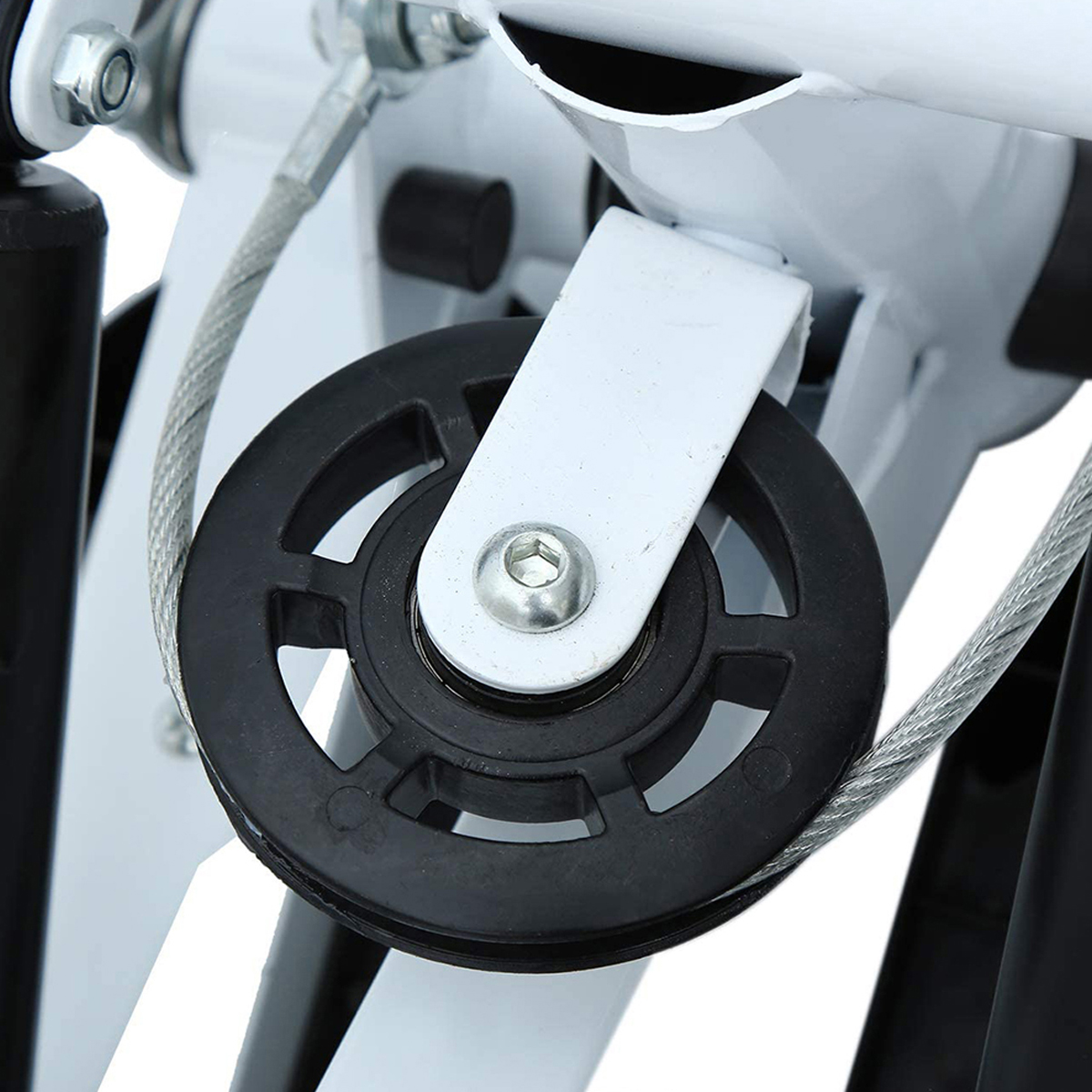 Primer plano de una polea negra con un soporte blanco y un cable plateado. La polea es parte de una máquina.