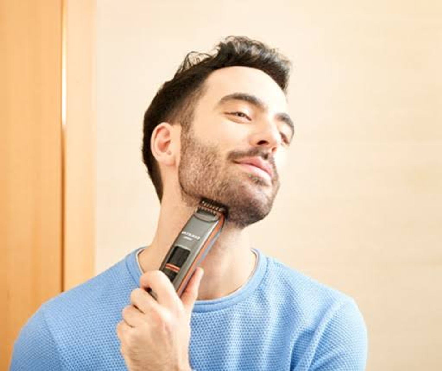 Hombre usando un recortador de barba. Se está recortando el cuello. El recortador es negro y plateado.