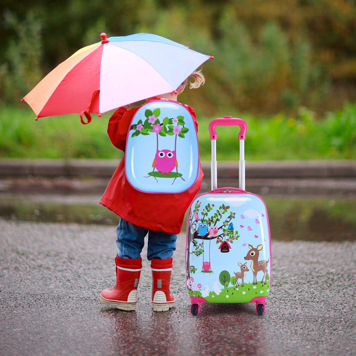Kind unter Regenschirm, mit Rucksack und Koffer. Regentag, verschwommener Hintergrund. Bunt.