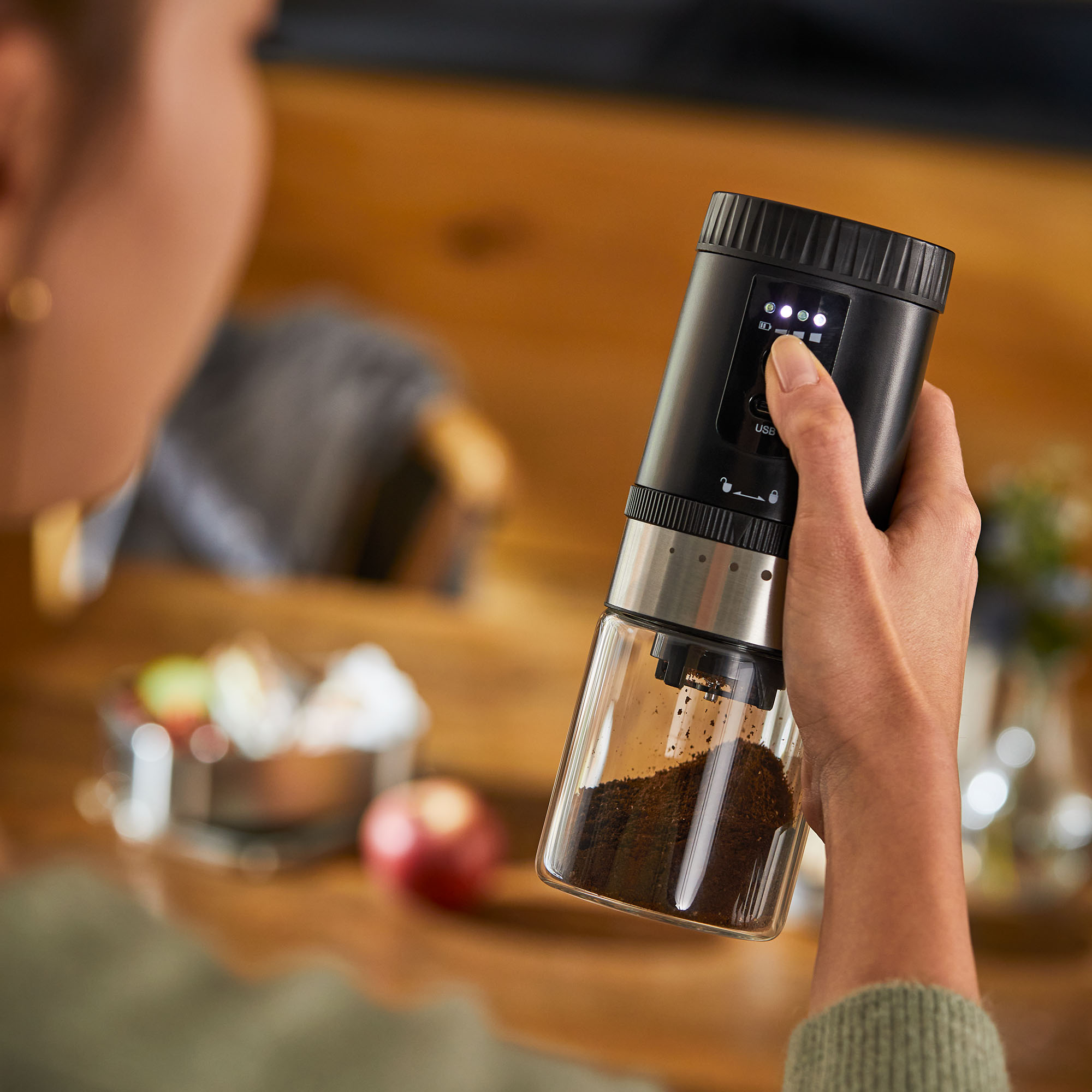 Eine Frau, die eine schwarz-silberne elektrische Kaffeemühle hält, Kaffeesatz sichtbar.