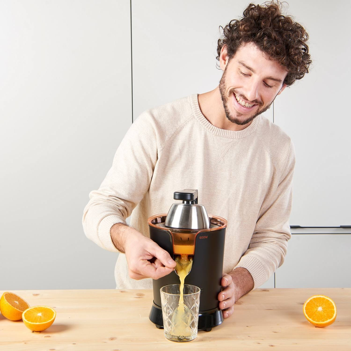 Un uomo versa il succo in un bicchiere da un estrattore nero, con arance su un tavolo di legno.