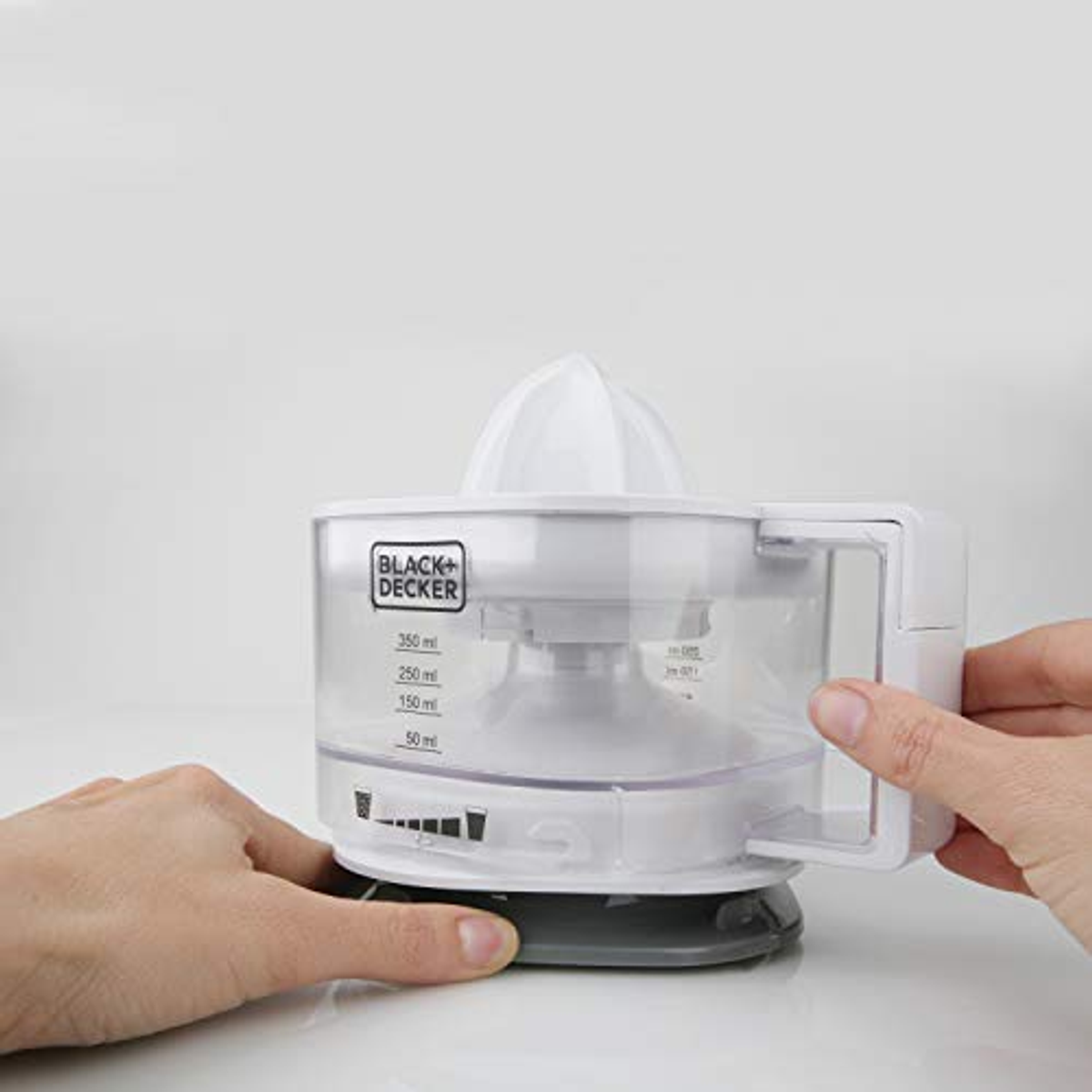 A white juicer with a clear container, held by hands. The Black+Decker logo is visible.