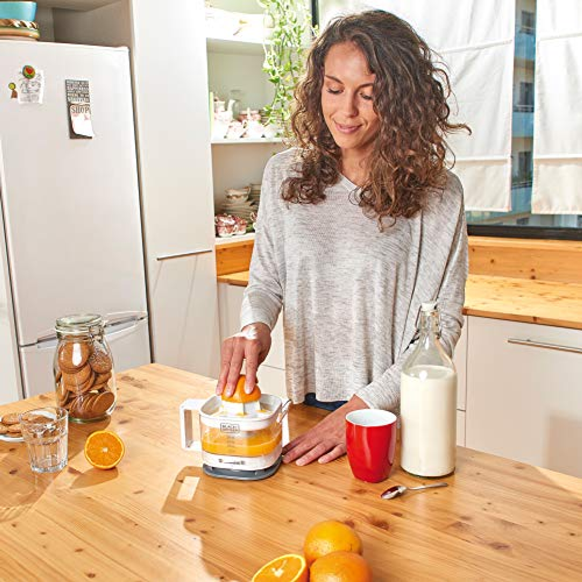 A woman squeezing oranges with a citrus juicer on a wooden table in a kitchen.