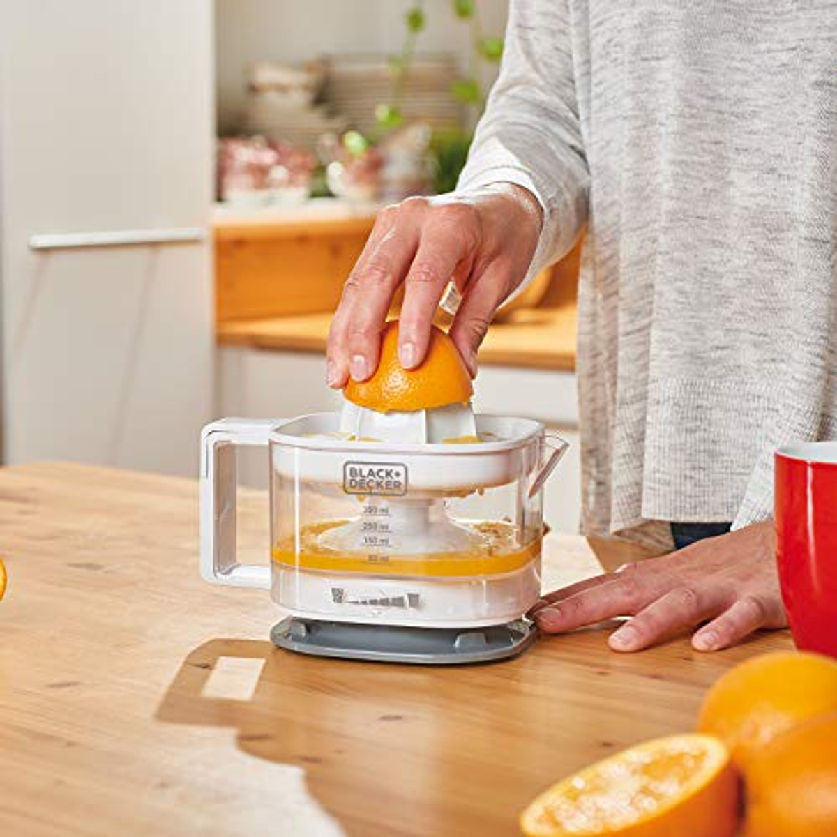 Woman squeezing orange half into a juicer, counter and oranges visible.
