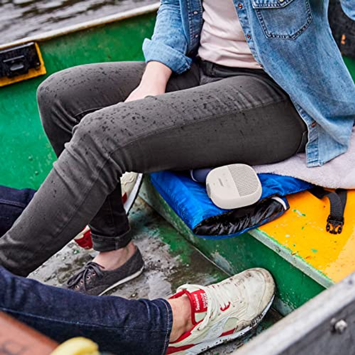 Osoba w łodzi z głośnikiem na kocu. Widoczne buty.